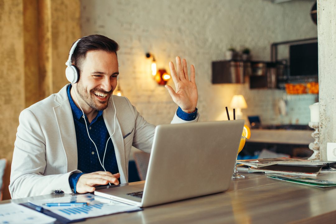 Man waiving to a laptop screen with a big smile